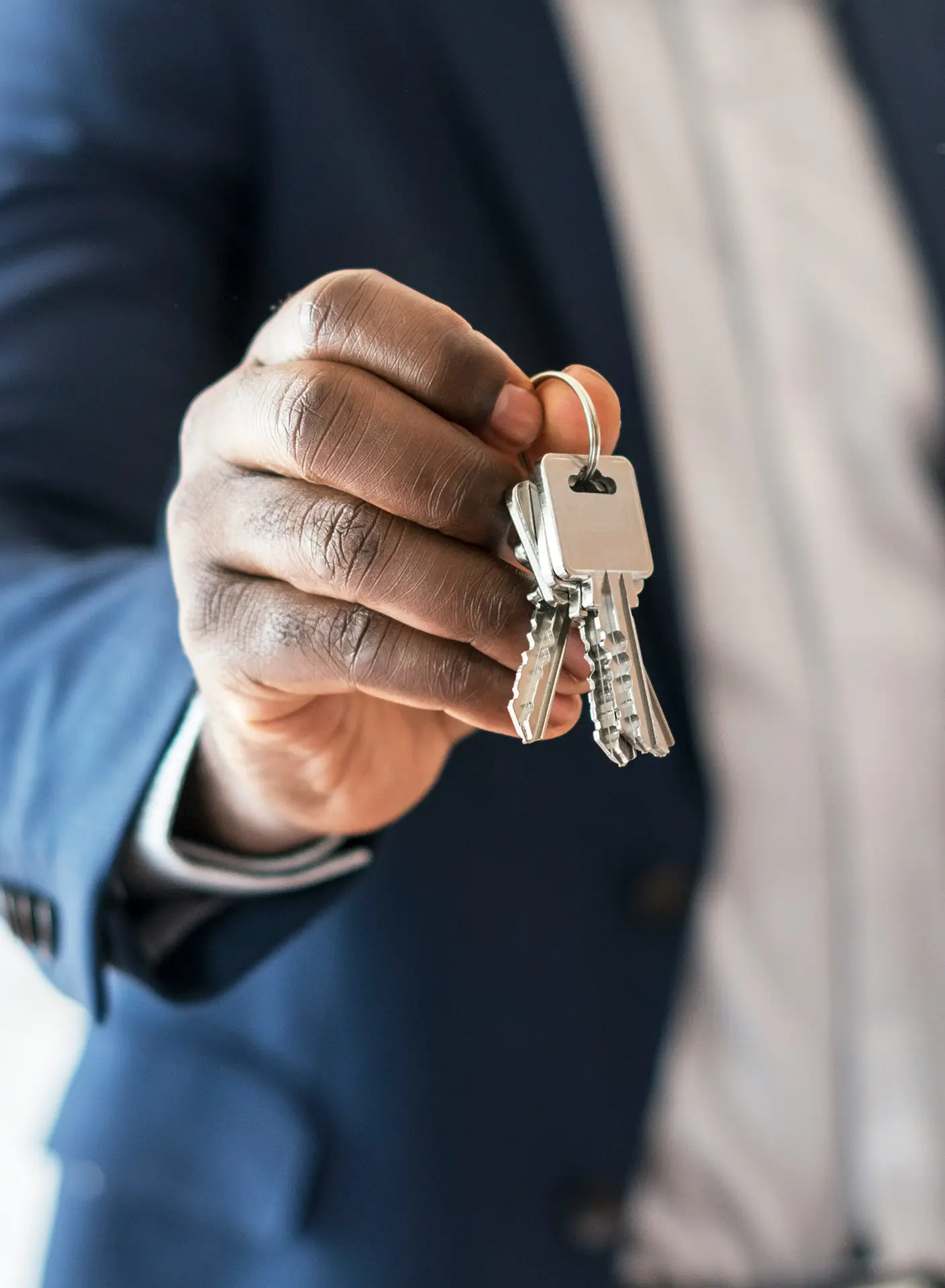 Person in blue suit holding a silver keyring with several keys toward the camera.